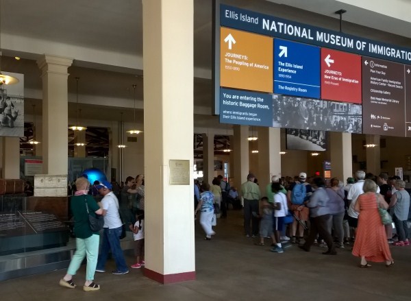 Visitors in Baggage Room at Ellis Island looking at historic baggage, exhibits and interactive media.