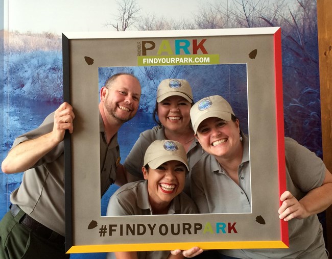 Three teachers pose with a ranger in a frame