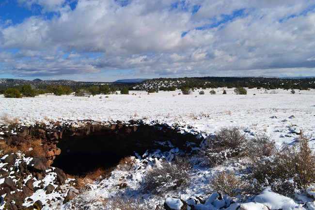 A thin layer of snow blankets the ground above a cave entrance.