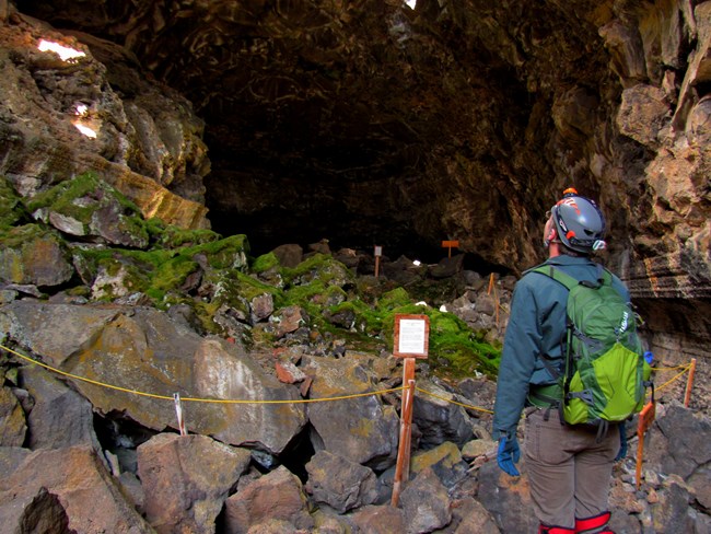 A caver stands in front of a roped-off mossy spot on boulders.