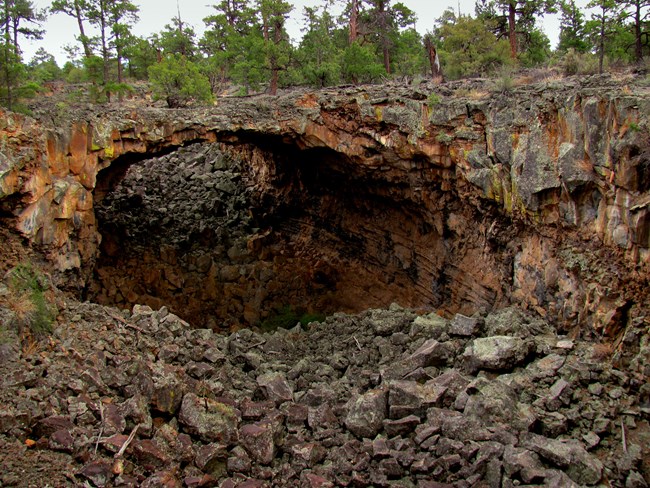 A wide rock trench with a reddish-black arc that forms a bridge between the trench walls.  The trench floor is covered with boulders.
