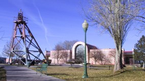 A metal frame creates a tall and narrow pyramid shape next to a single-floor building with a large windowed entrance.