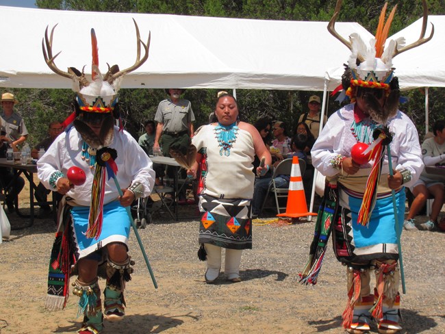 Three Pueblo members perform a dance in traditional dress.