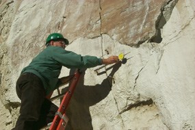 Image of a National Park Service volunteer using a measuring device to monitor a large crack in the rock.