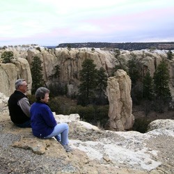 Two people sitting on a rock cliff overlooking a small canyon.