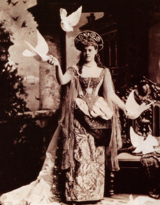 Alva in her Fancy Dress Ball Costume A woman in an elaborate costume, surrounded by fake birds.