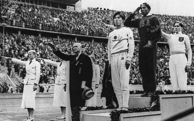 Men stand on a podium while others around the salute