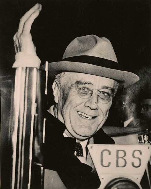 FDR Campaigning in 1944 A man wearing a hat waves as he stands in front of a microphone