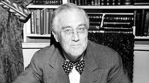 A man wearing a suit and a bowtie, seated at a desk