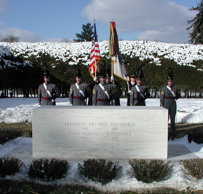 A group of cadets in uniform stand behind a gravestone