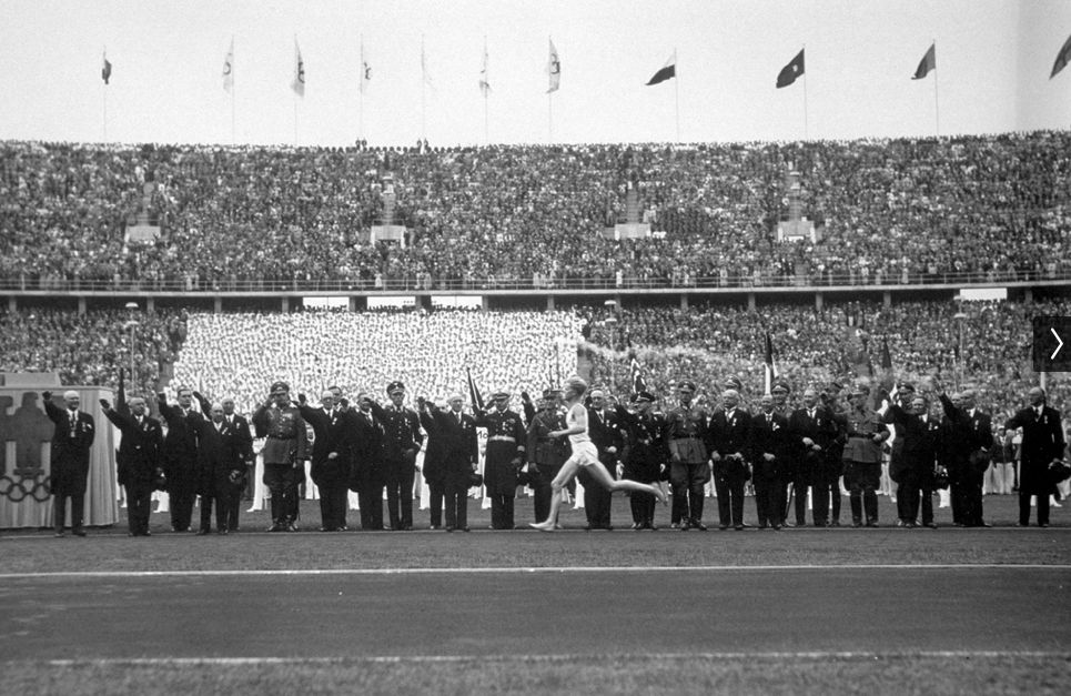 A man runs with a torch on a track while those alongside the track salute him