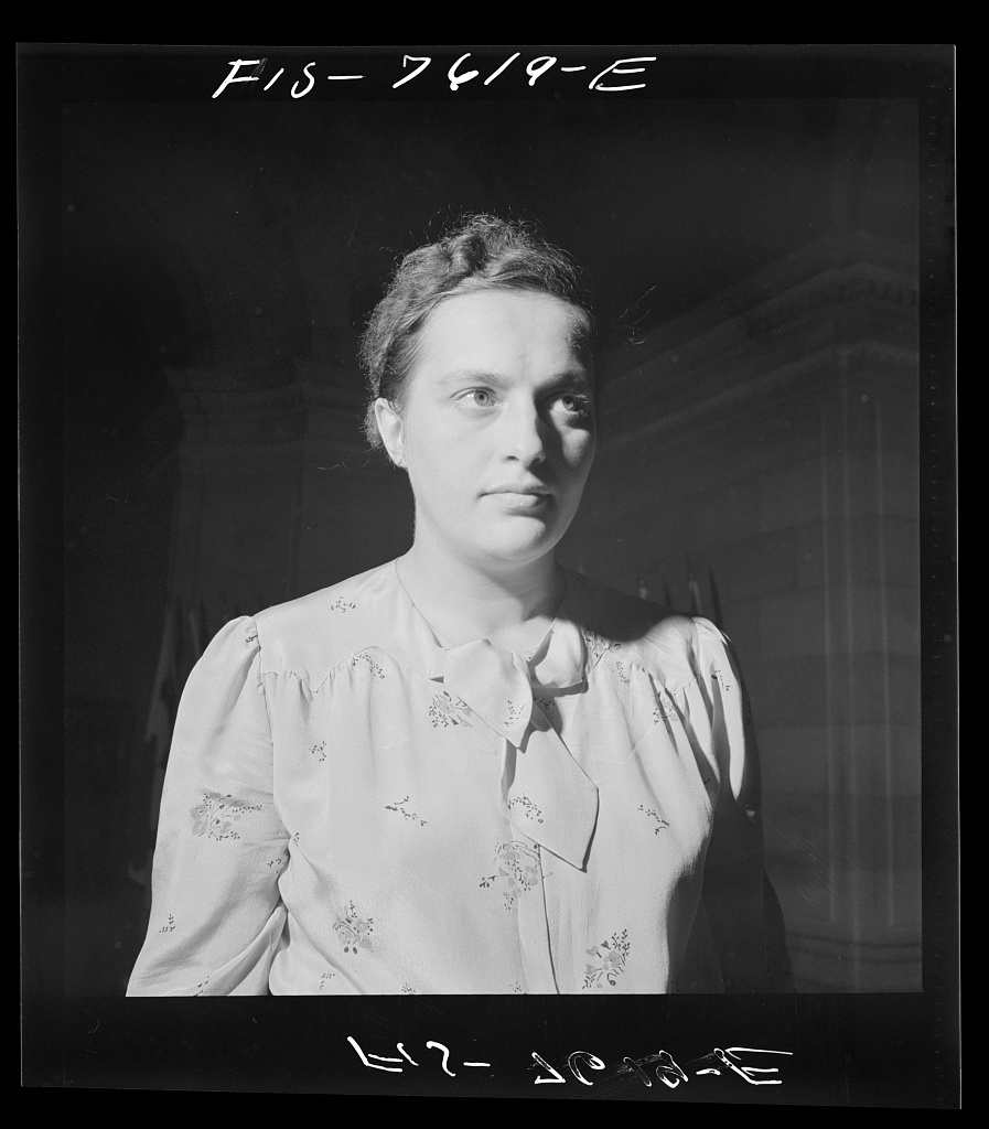 A young woman in a white shirt stands in sunlight