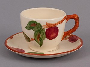 A cup and saucer decorated with apple and leaves, and a twig-form handle.