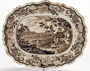 A brown and white platter decorated with printed river scene.