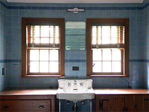 A room with ceramic tiles on the wall and a sink with mirror and two small windows on each side.