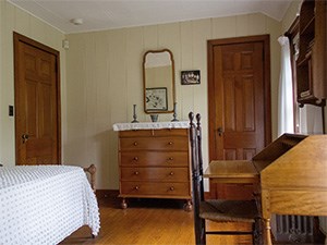 A small room with a single bed, desk, and chest of drawers.