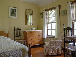 A small room with single bed, chest of drawers, and upholstered chair.