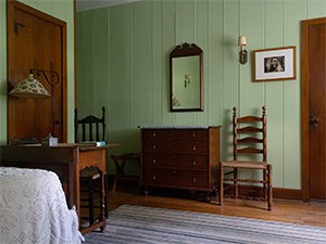 A small room with a wood desk and wood chest of drawers.