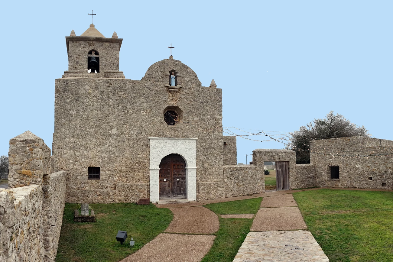 Stone church with a grassy area in front of it and walls to either side.