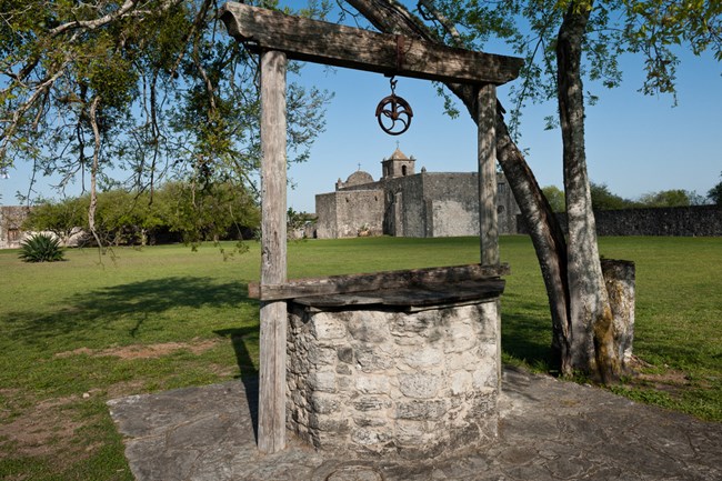 A stone well sits in front of a distant stone fort.