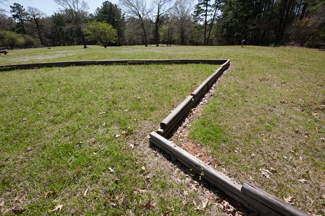 A low lying cement curb delineates the boundaries of an old fort, in a grassy field.