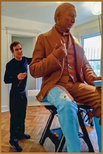 Un hombre se para al lado de una escultura de tamaño doble de Benito Juárez. Está tomando forma en barro.