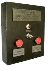 Caja negra ceremonial con placa, una pequeña luz eléctrica, interruptor con llave, y dos botones rojos.