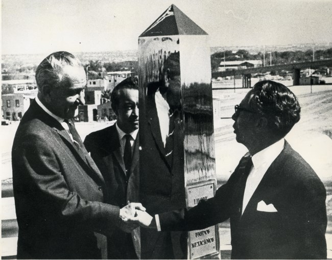 Los presidentes Johnson y Díaz Ordaz se dan la mano frente a un monumento cromado.