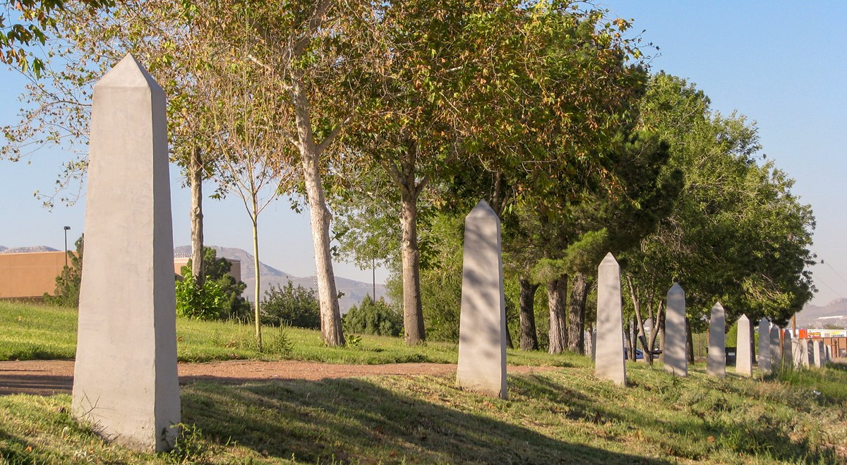 Una línea de postes de hormigón en forma de obeliscos se extiende hacia la distancia al lado de un sendero.