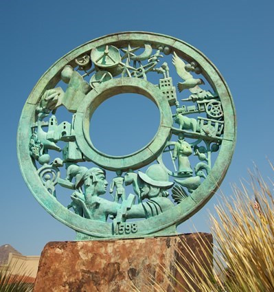 sculpture of green wheel with images of spaniards fighting the natives
