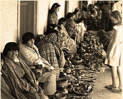 old photo showing a line with indigenous people selling goods outside the Palace of Gobernors