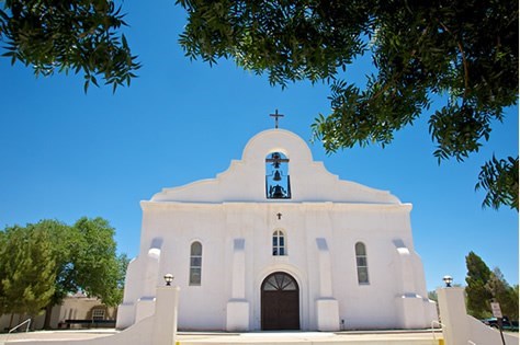 white, old spanish style  church, with a cross on top and a bell in the middle