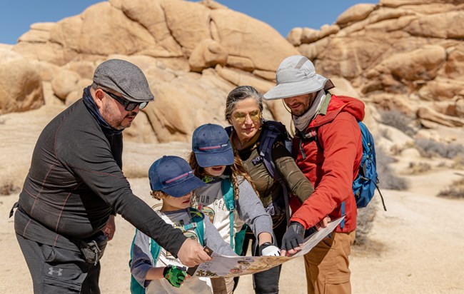 Una familia usando un mapa alrededor de formaciones rocosas y plantas deserticas.