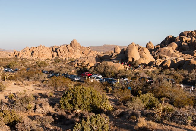 Varios autos estacionados junto a la carretera con muchos visitantes escalando las rocas.