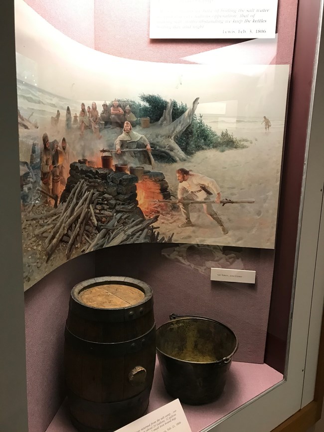 Una representación artística del proceso a elaborar sal del agua del océano y una  réplica de un barille y un balde