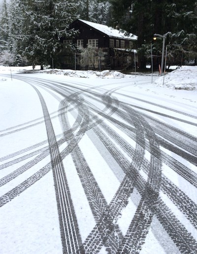 Huellas de neumáticos entrecruzan una carretera nevada enfrente de un edificio rústico.