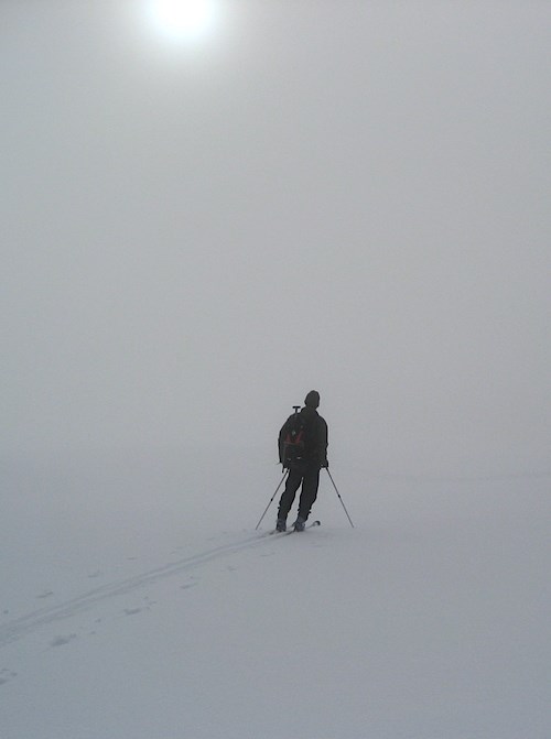Un esquiador se detiene en una pendiente nevada mientras la niebla cubre el paisaje.