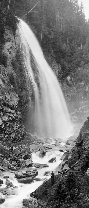 Una foto antigua en blanco y negro de una cascada con un hombre parado a su pie.