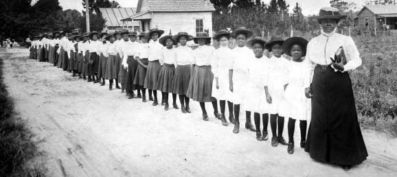A nurse and two school agents pose in front of The Booker T. Washington Agricultural School on Wheels