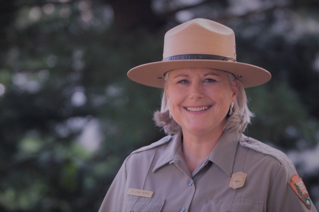 An older woman in a ranger uniform smiles at the camera.