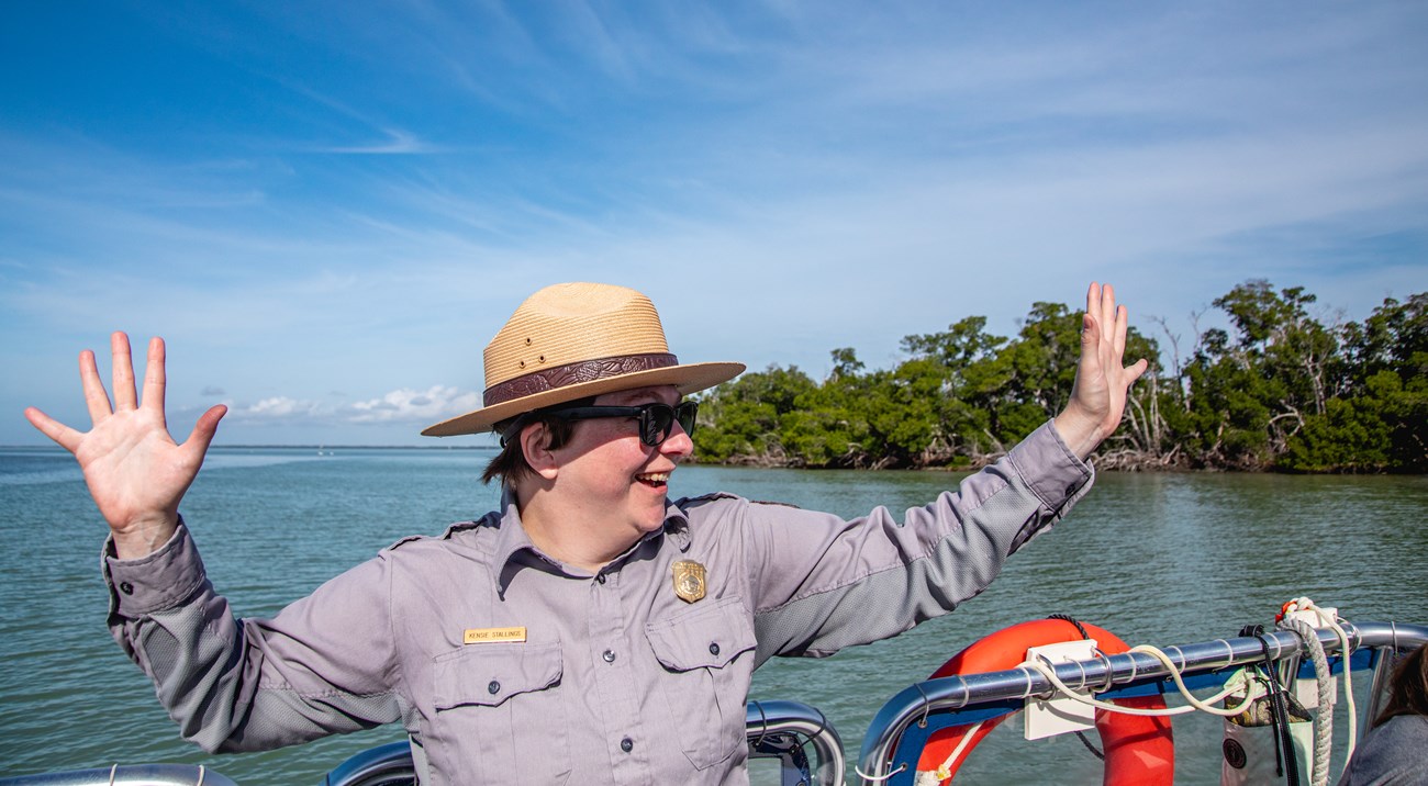 A Park Ranger on a boat holds our their arms, expressing joy.