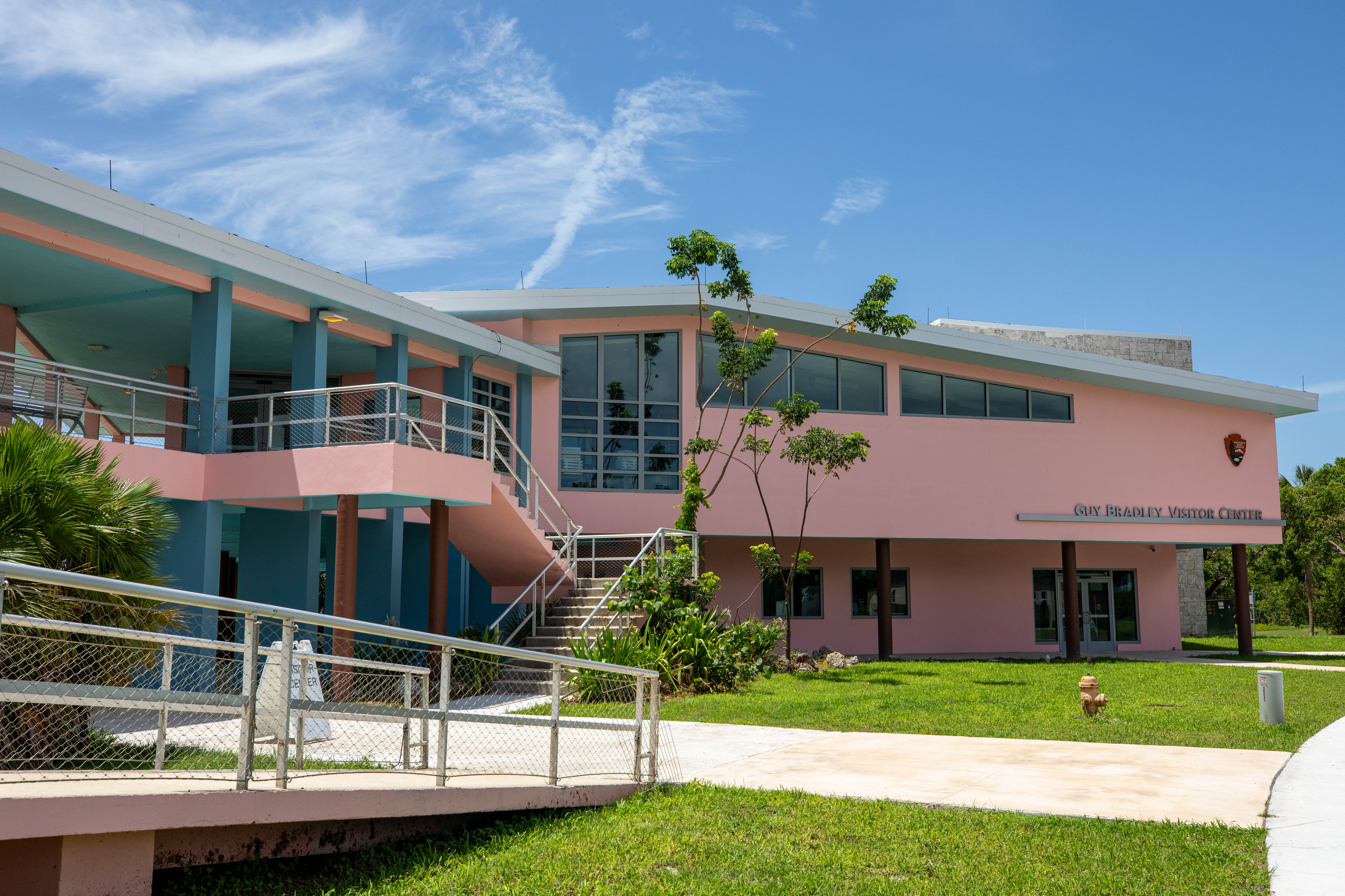 Pink two-story building with ramp. Building displays NPS arrowhead logo and words Guy Bradley Visitor Center