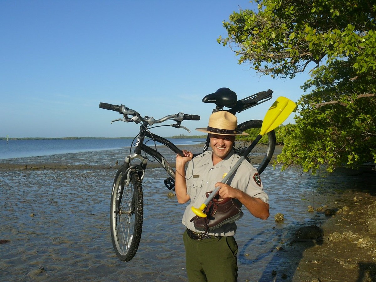 Park ranger holds up a paddle, bike and hiking boot.
