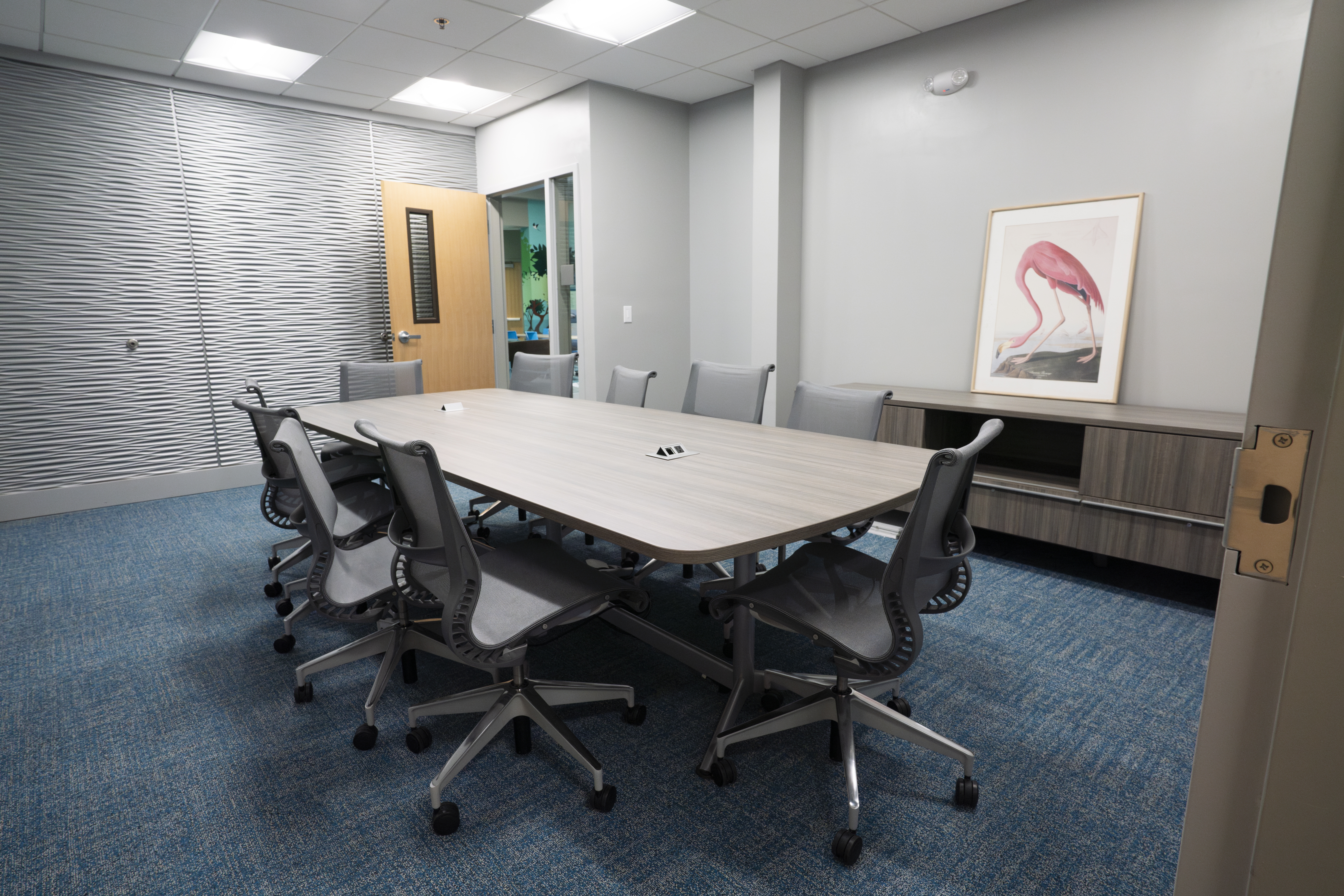A large gray table with several chairs situated in the middle of a small conference room