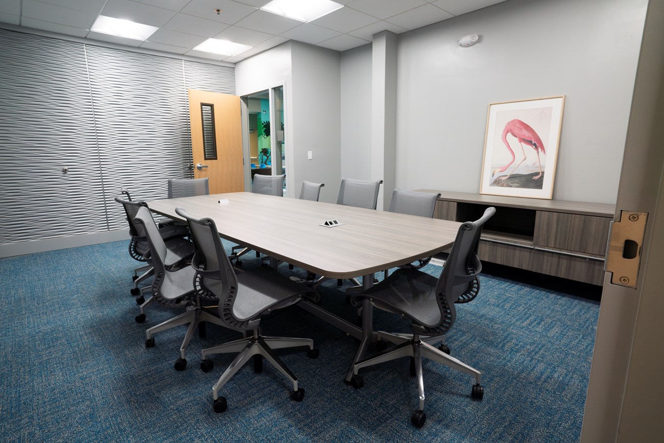 A large gray table with several chairs situated in the middle of a small conference room