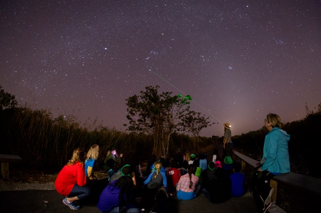 A park ranger pointing at stars with students sitting on the ground