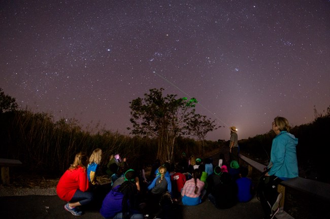 A park ranger pointing at stars with students sitting on the ground