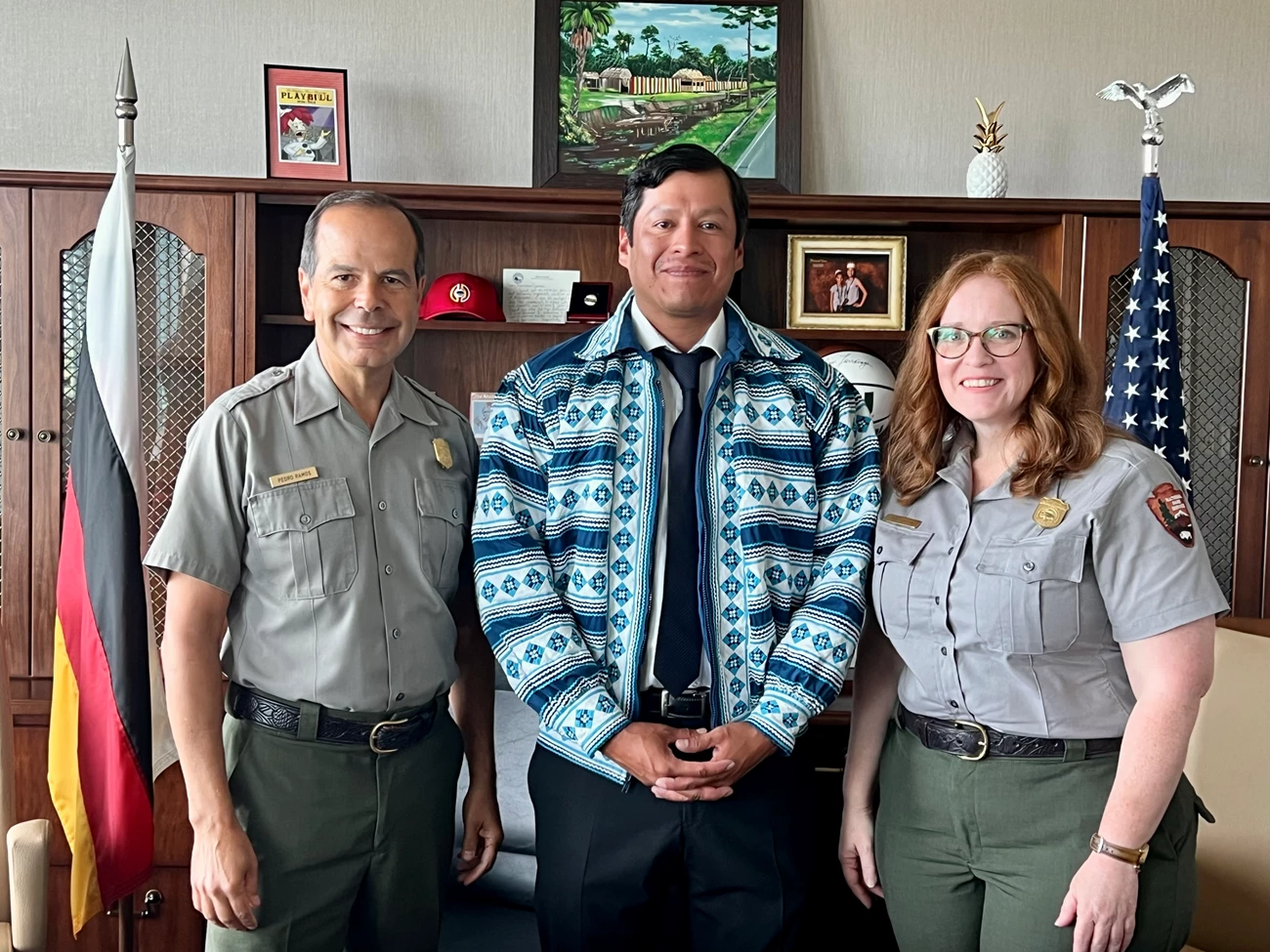 National Park Service and Miccosukee Tribal representatives From left to right, a uniformed male park ranger, a Miccosukee Tribal official in traditional jacket, and a female uniformed park ranger stand in an office.