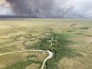 An aerial view shows a fire burning in the distance with a road and observation tower towards the front.