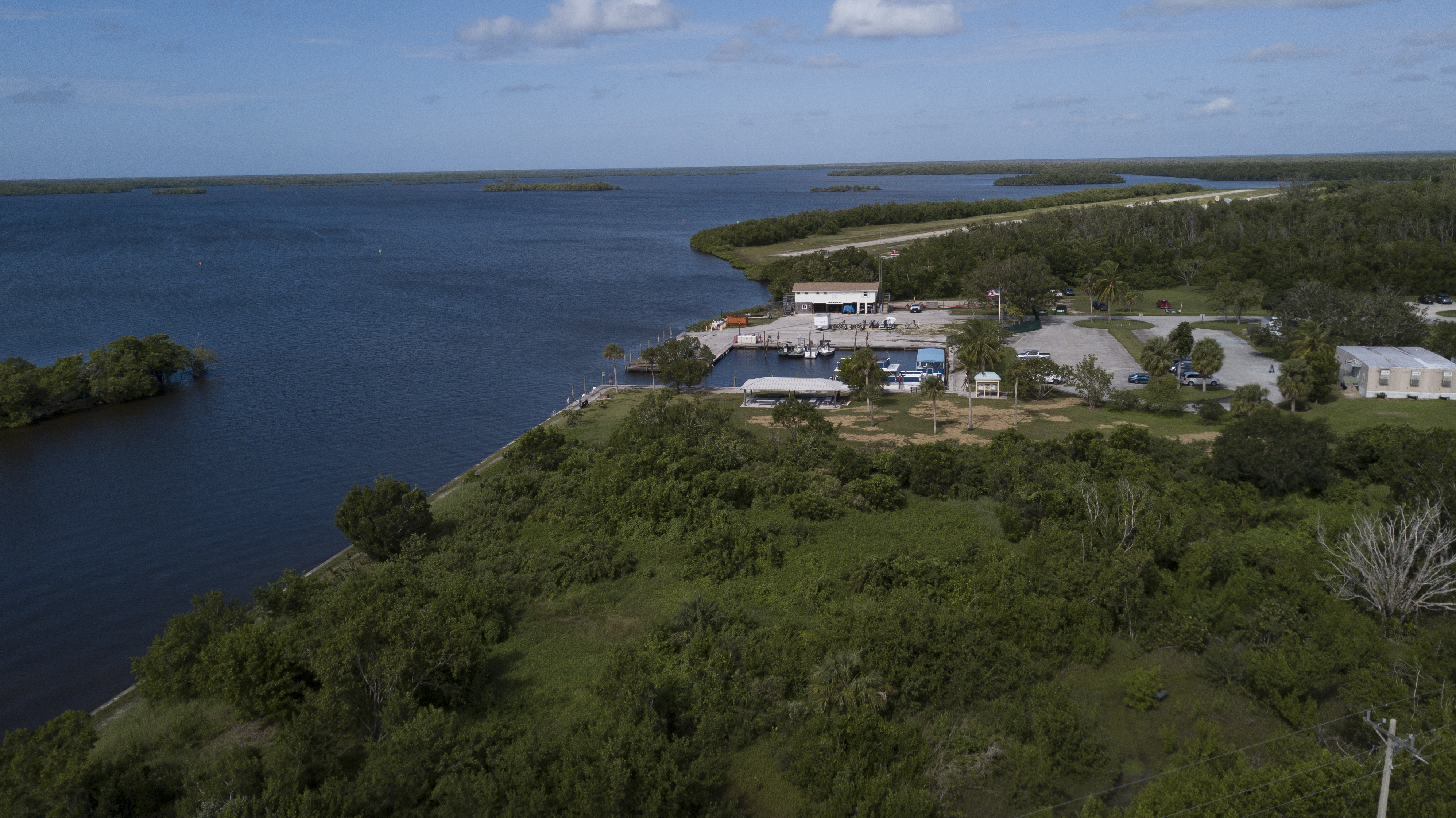 An aerial view of the vegetated coastline on Chokoloskee Bay with a cut-out boat basin surrounded by buildings and a parking lot.